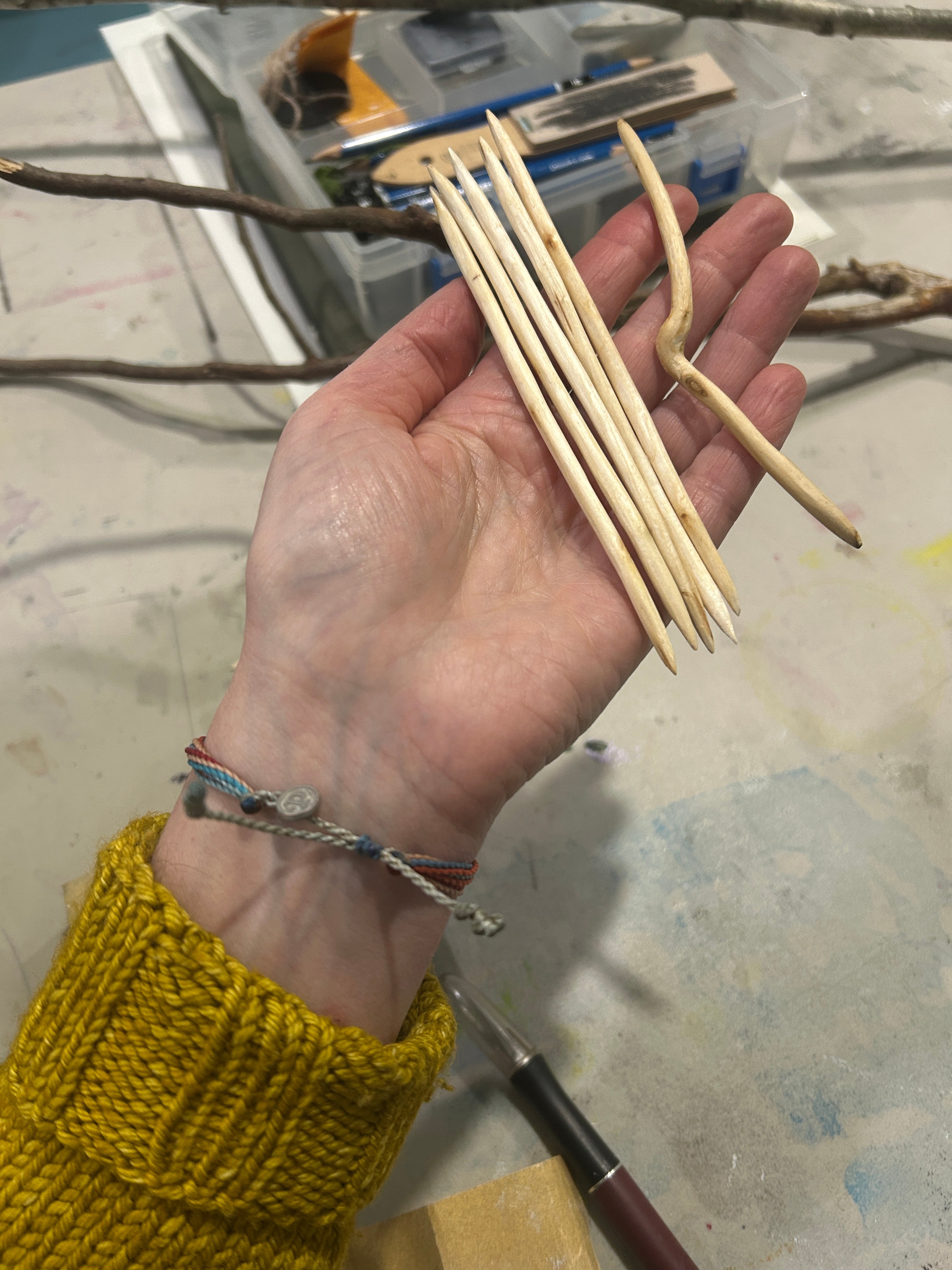 Woman's hand holding hand carved knitting needles and a cable needle made from branches from Paperbark Maple and River Birch trees in North Carolina. 