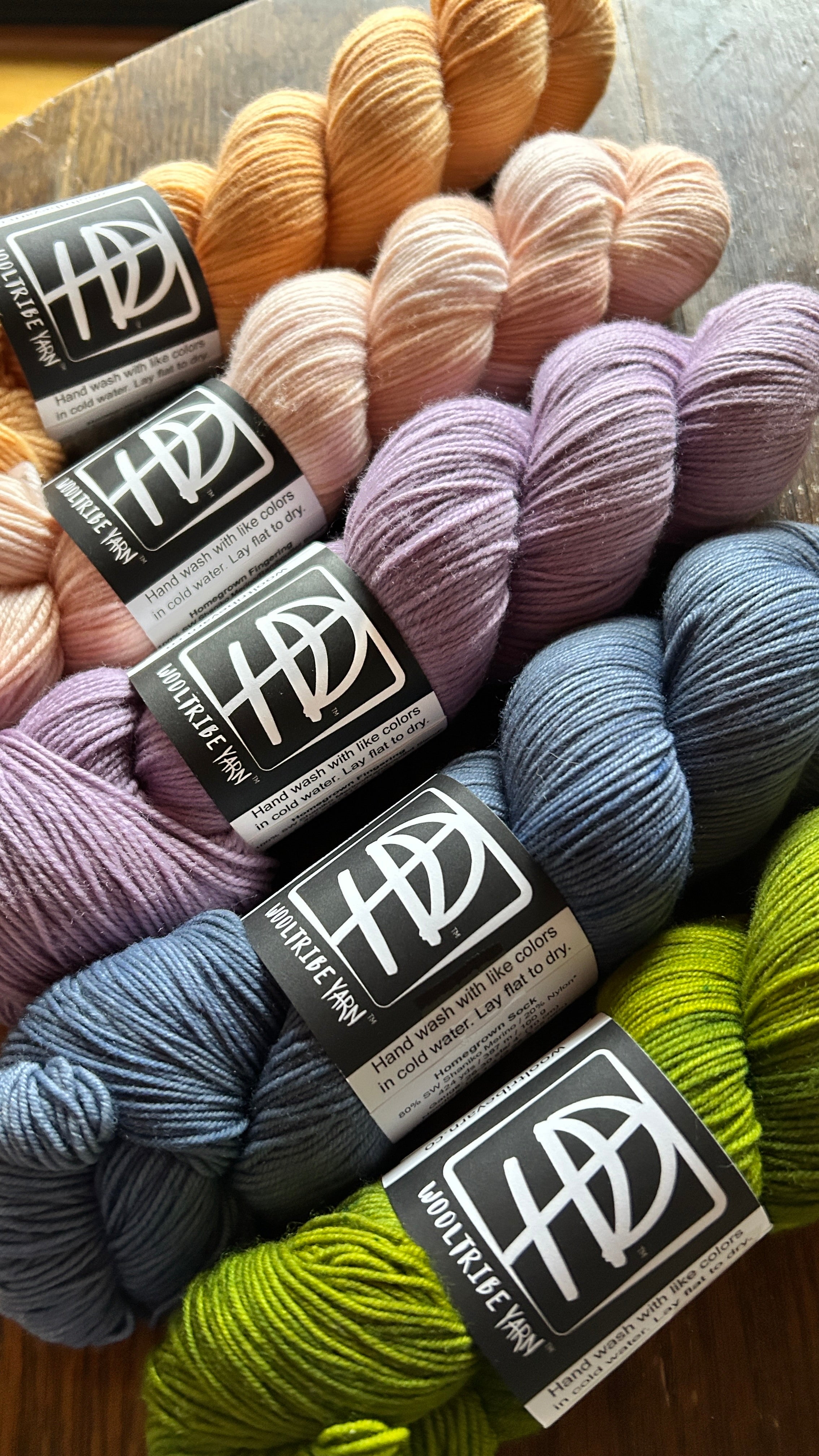 Five skeins of WoolTribe hand dyed yarn made using Shaniko Wool featuring 100% USA merino fiber. Colors shown from left to right are naturally dyed Onion Skin peach, Tiffany Rose, Naturally Dyed Logwood lavender, Kyanite blue, and Hellbender green.